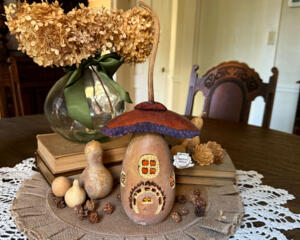 A mushroom house made from natural gourds. The original gourd stem on the top. A "Squirl Cottage" house sign hangs on the side. 